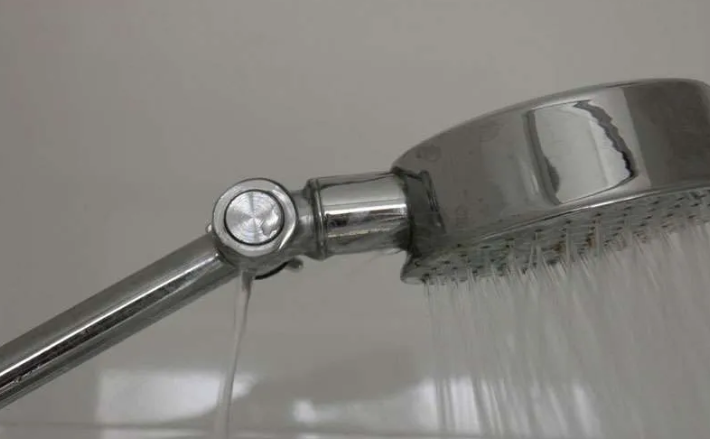 pommeau de douche en métal avec fuite d’eau sur le côté, montrant un problème plomberie à réparer pour éviter le gaspillage.