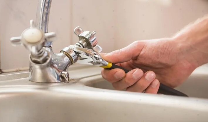un plombier serrant un robinet avec une pince pour réparer un problème plomberie et stopper une fuite.