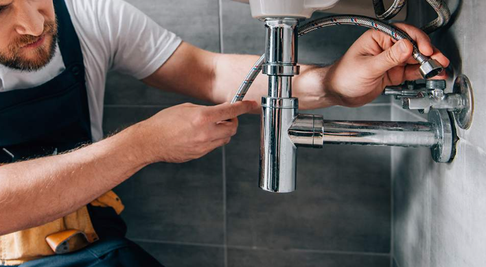 un plombier réparant un siphon sous un lavabo avec un tuyau flexible, illustrant la résolution d’un problème plomberie pour stopper une fuite.